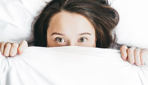 young woman in bed, pulling sheet over her face